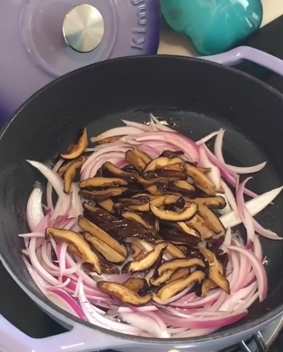 Sliced shiitake mushrooms placed on top of red onions in a purple pan.