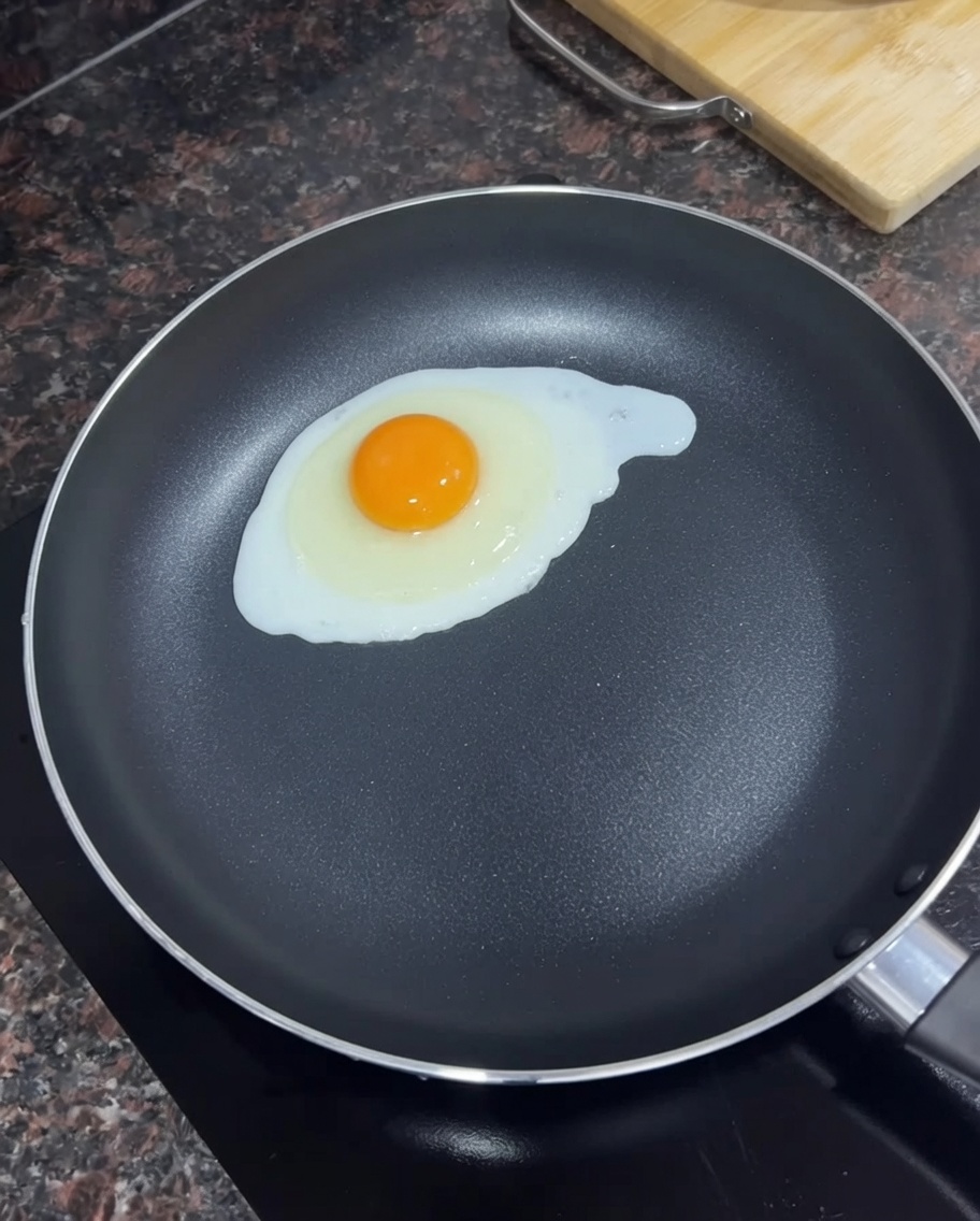 A single egg frying in a black skillet with melted butter.