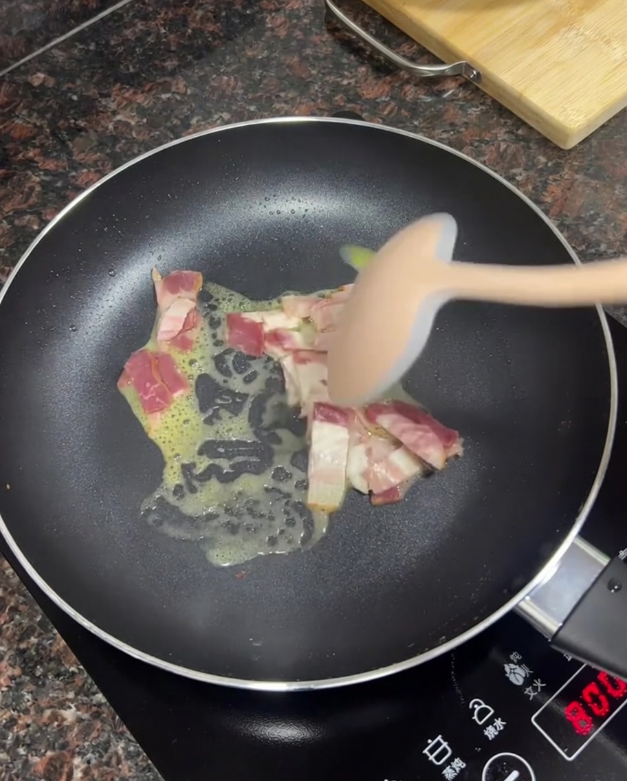 Bacon pieces frying in melted butter in a skillet.