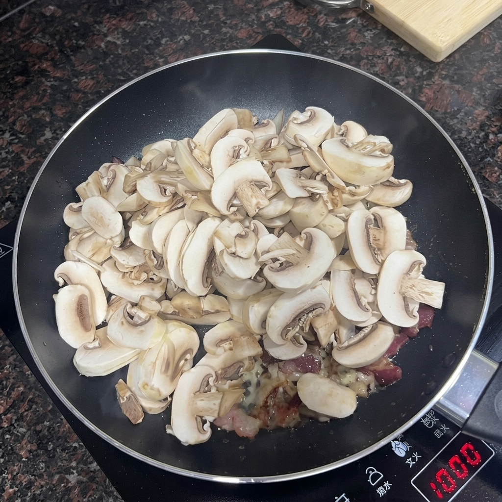 Sliced button mushrooms being added to a pan with bacon and garlic.