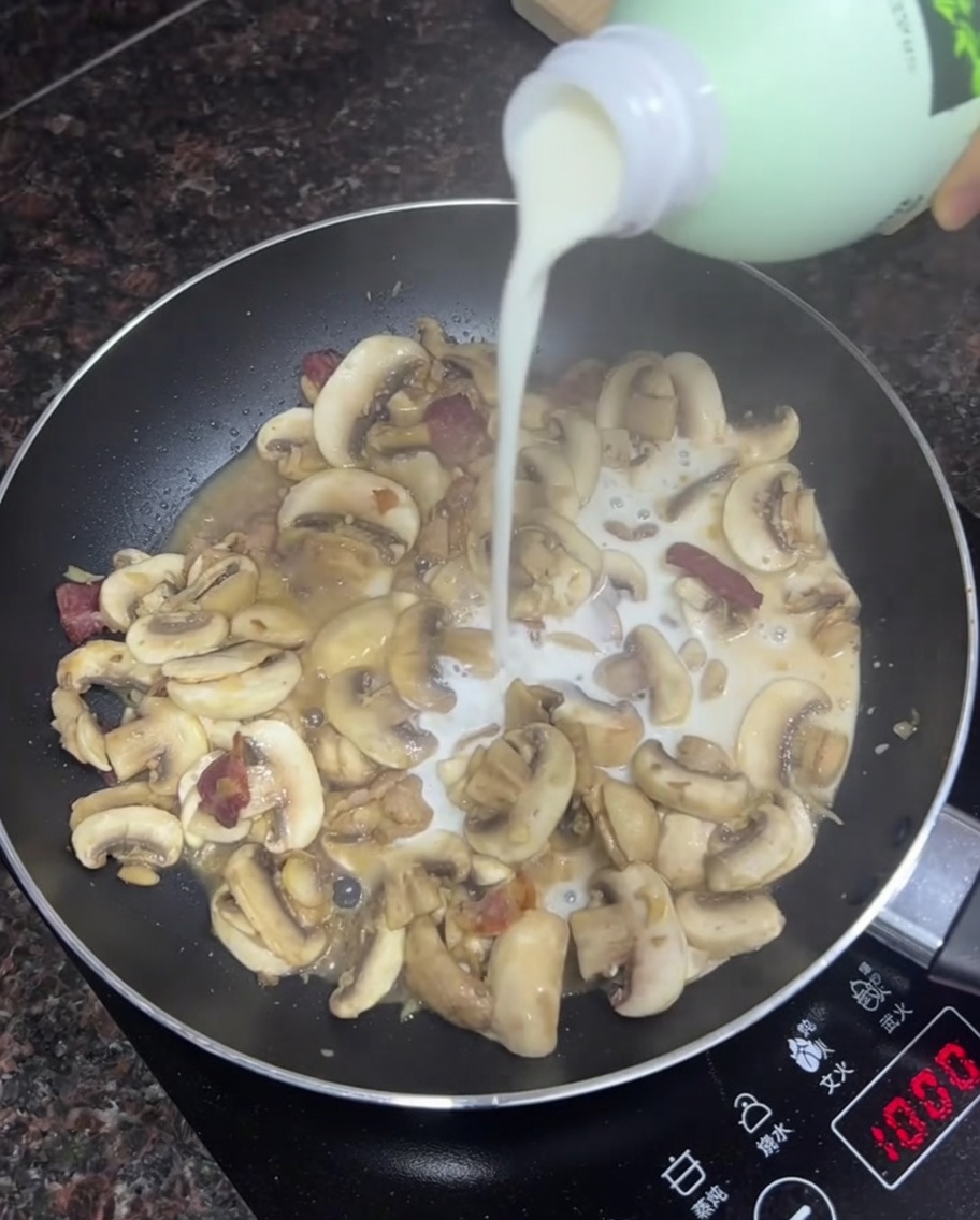 Milk being poured into a skillet with sautéed mushrooms and bacon.