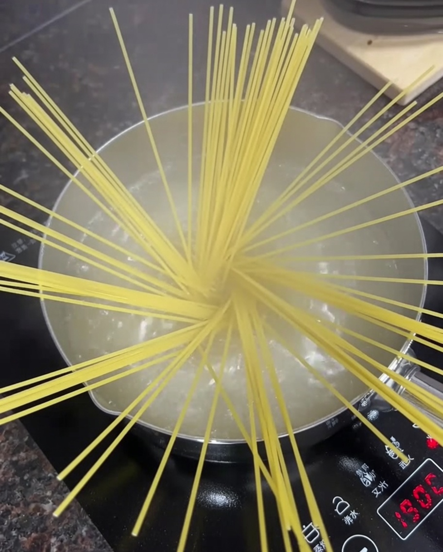 Dry spaghetti noodles spread out in a pot of bubbling hot water on a stovetop.