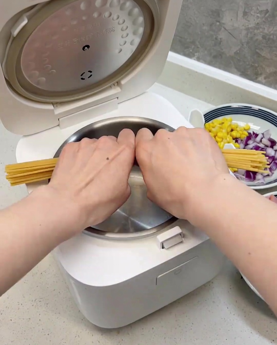 Spaghetti noodles broken in half, neatly arranged inside the clean rice cooker bowl.