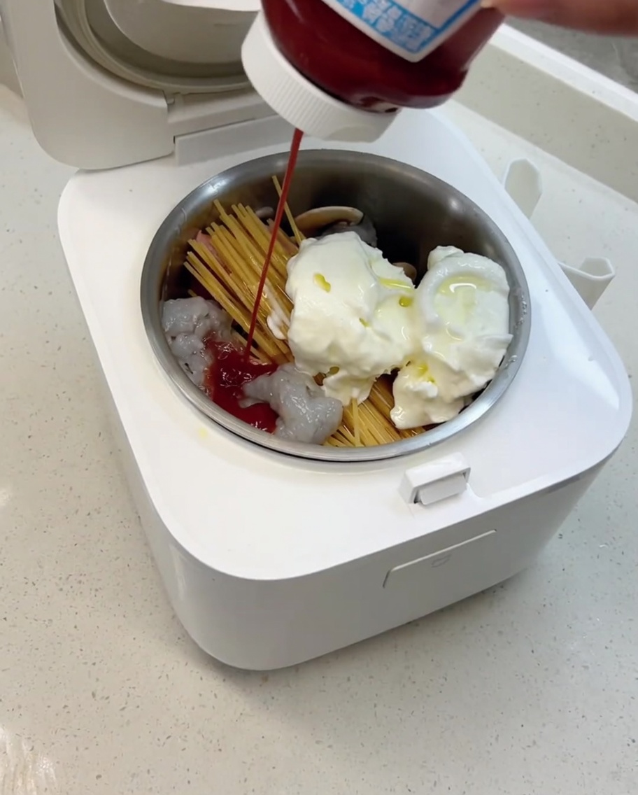 Olive oil and tomato sauce being poured into the rice cooker pot, ready to be cooked with the other ingredients.