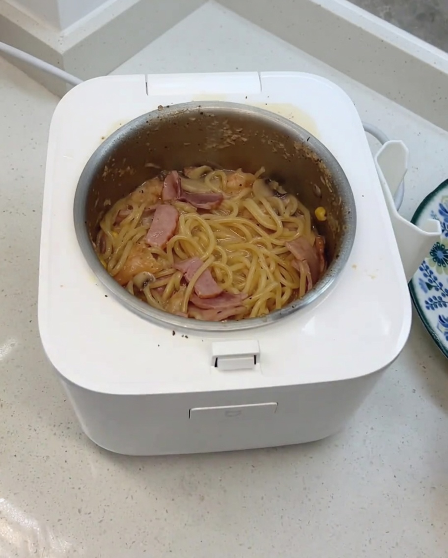 The finished creamy mushroom spaghetti being stirred with added cheese and dairy cubes in the rice cooker.