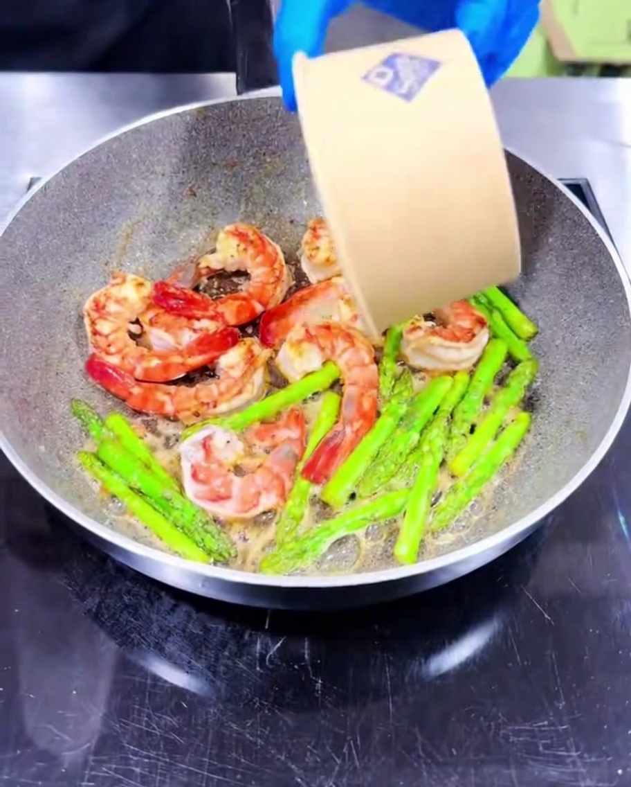 Minced garlic being stirred into the pan with the cooking shrimp and asparagus.
