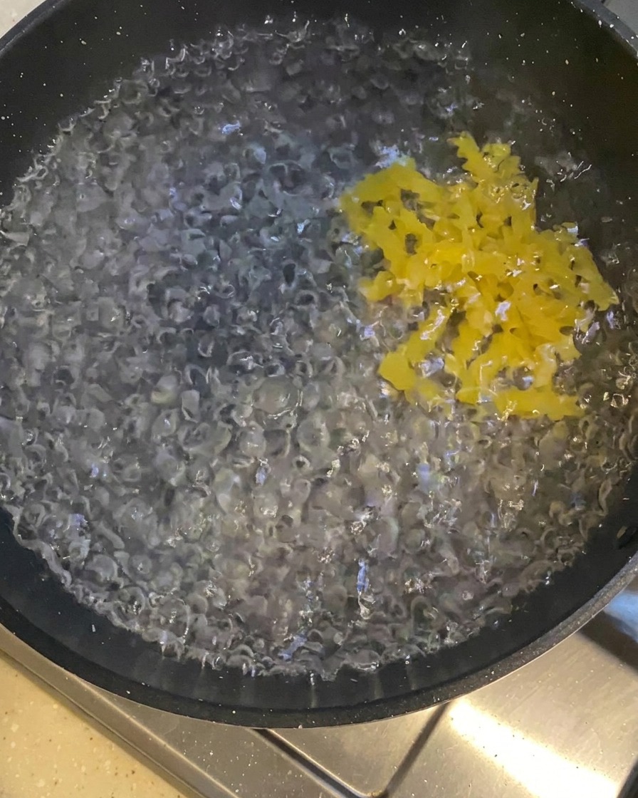 Yellow curly pasta being added to a dark pot filled with vigorously boiling water.