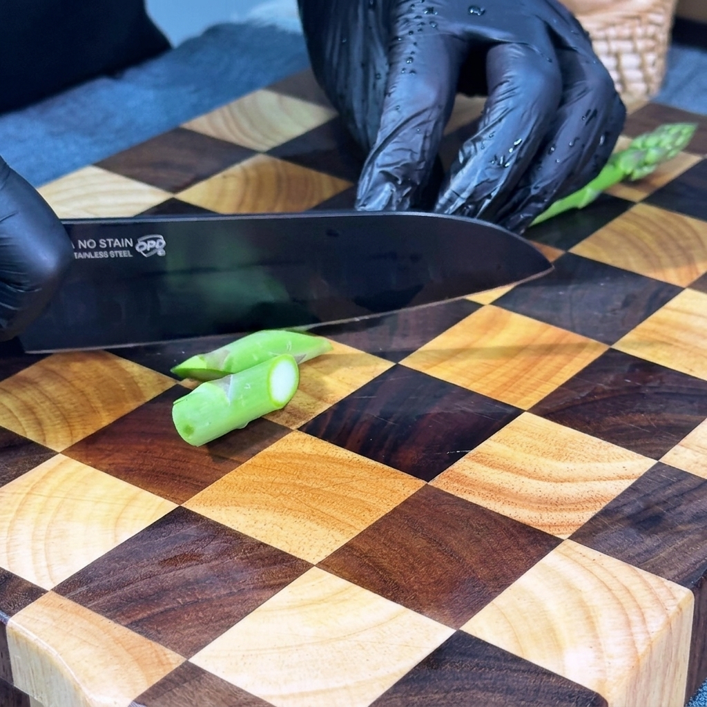 Fresh asparagus stalks being sliced into small, uniform diagonal pieces on a wooden cutting board.