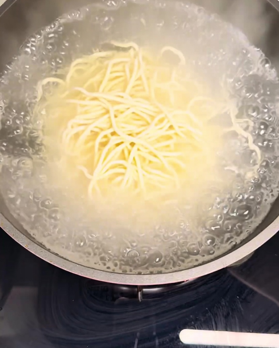 Fresh noodles submerged in a pot of vigorously boiling water.