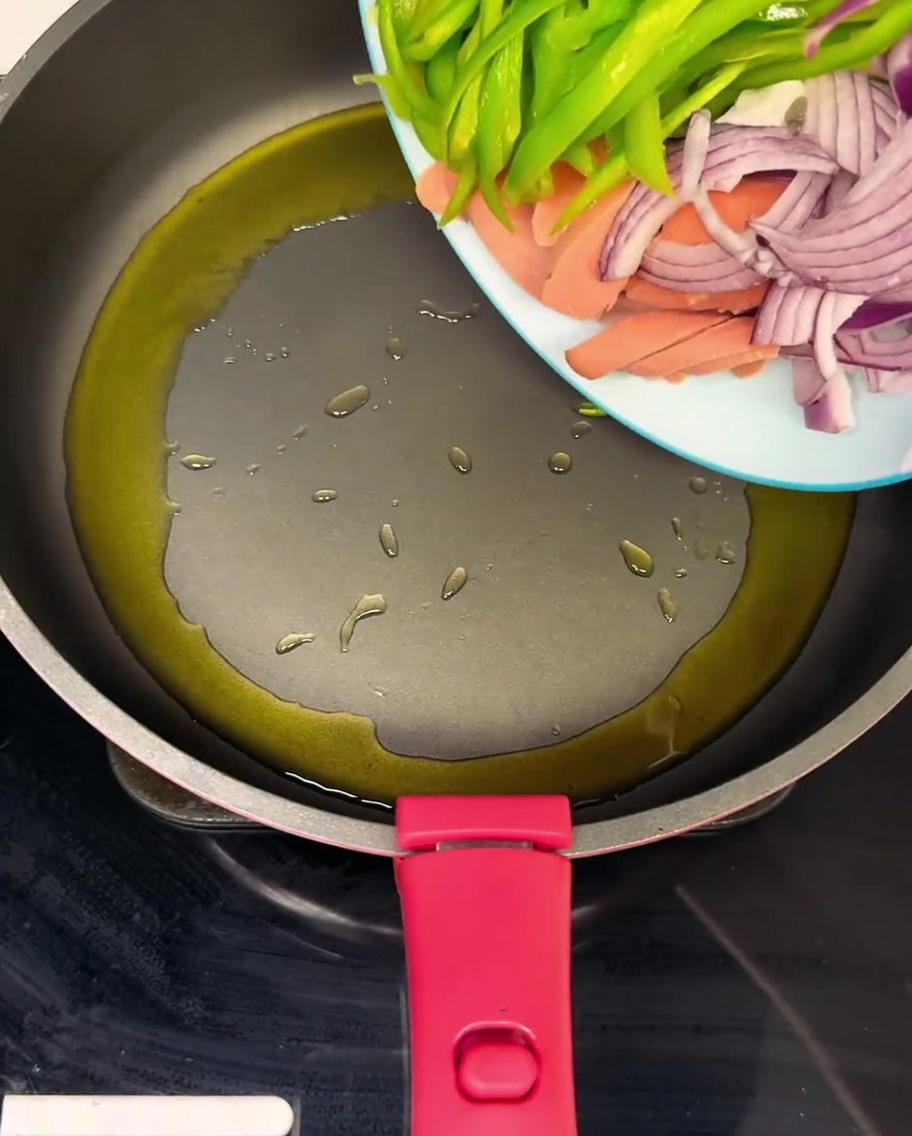 A hot pan containing sliced ham, green bell peppers, and onions being tossed in oil.