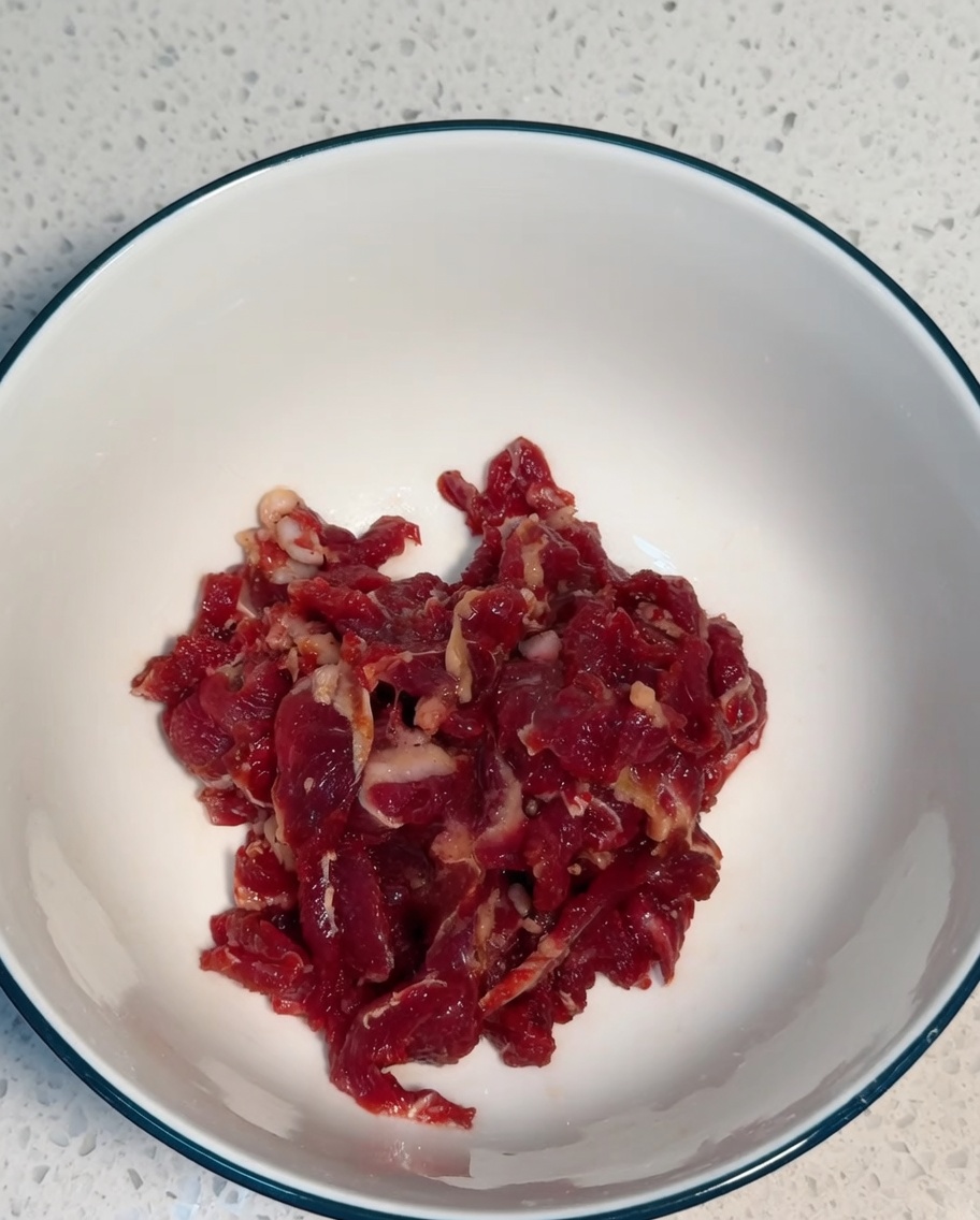 Thinly sliced beef being thoroughly combined with marinade ingredients in a white bowl.