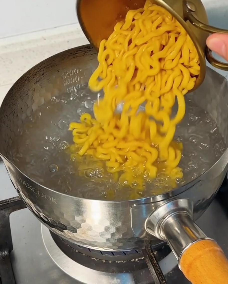 Macaroni pasta being poured into a pot of bubbling boiling water.