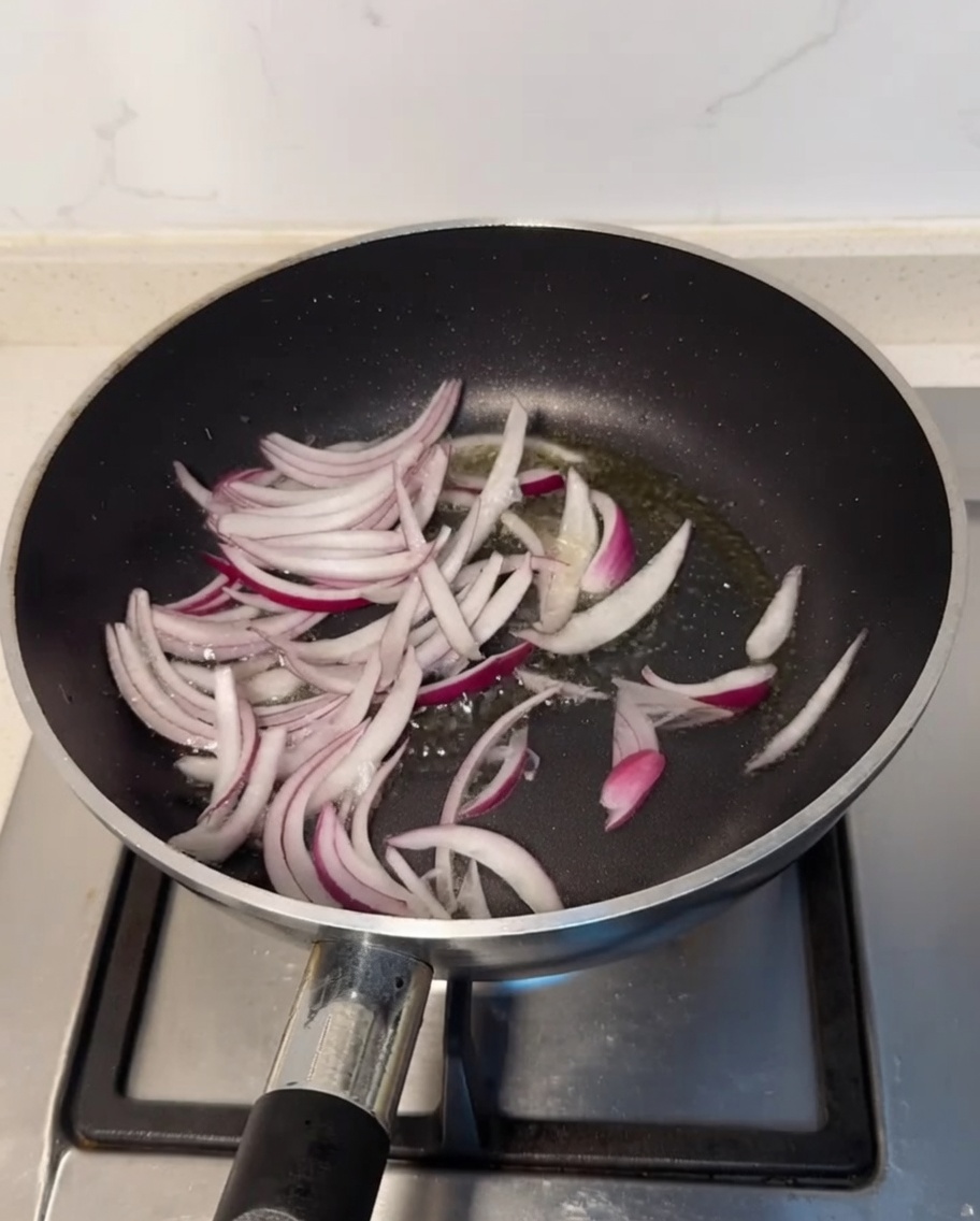 Sliced purple onion pieces sizzling in a pan with hot cooking oil.