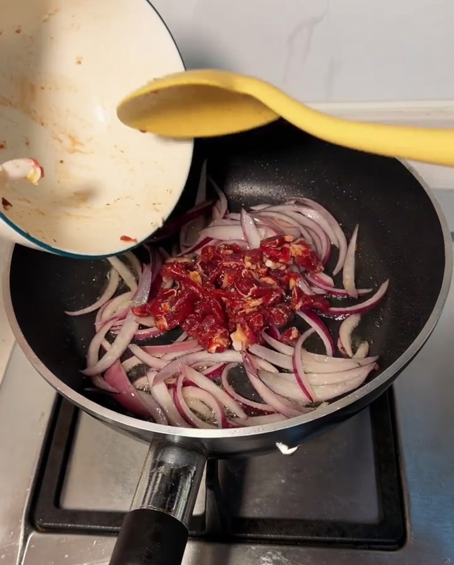 Marinated beef being added to the pan and mixed with the softened onions.