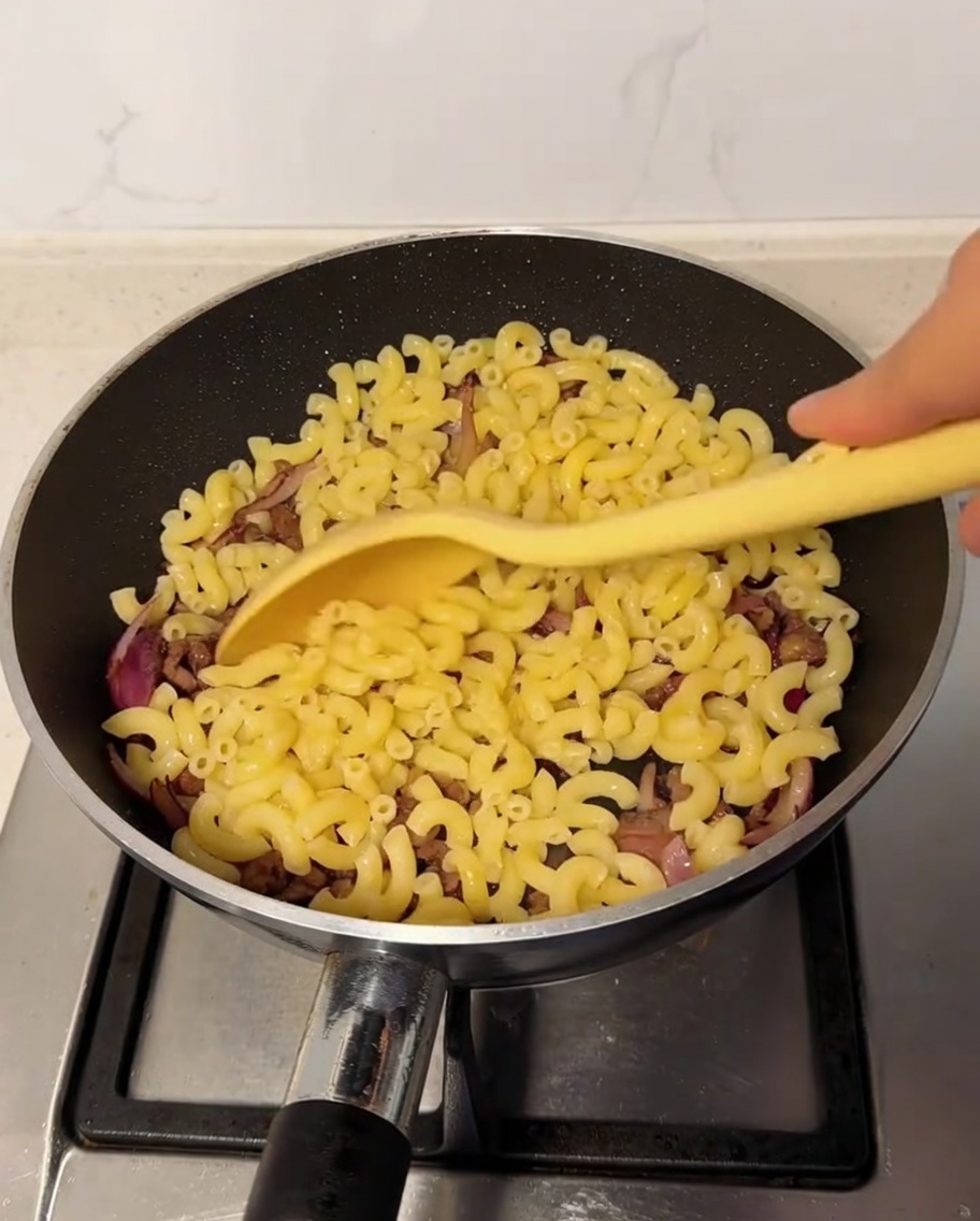 Cooked macaroni being incorporated into the pan with the beef and onion mixture.
