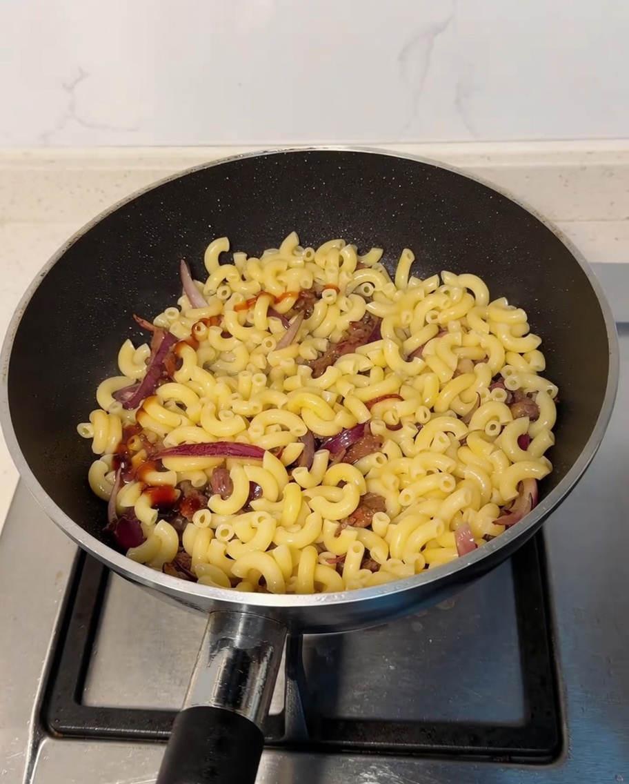 Oyster sauce and light soy sauce being drizzled over the macaroni and beef mixture in the pan.
