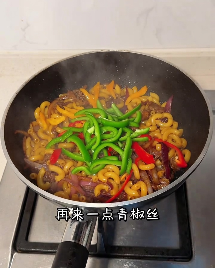 Sliced green bell pepper being stirred into the pan with macaroni and beef.
