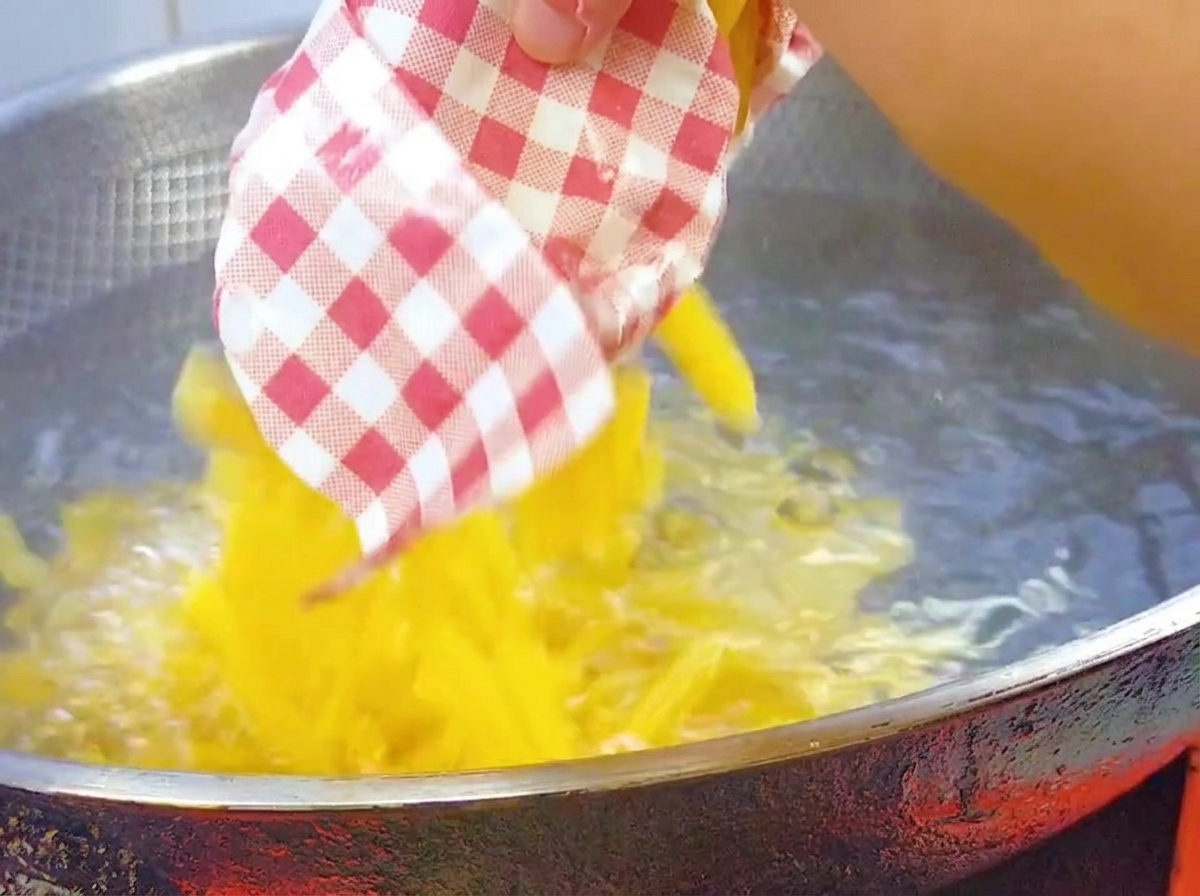 Dry penne pasta being poured into a large, boiling wok of salted water.