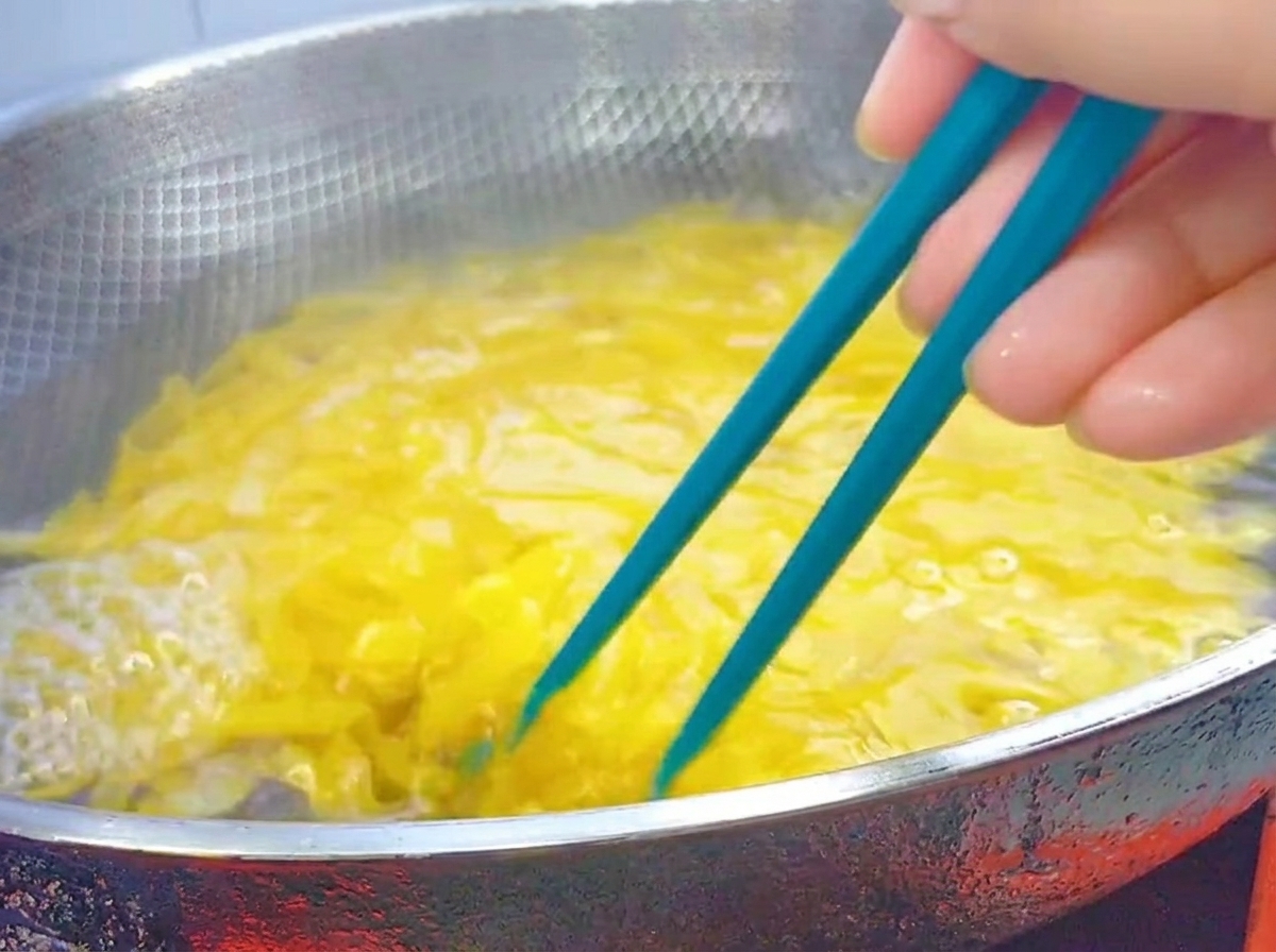Blue chopsticks stirring boiling penne pasta in a large stainless steel wok.