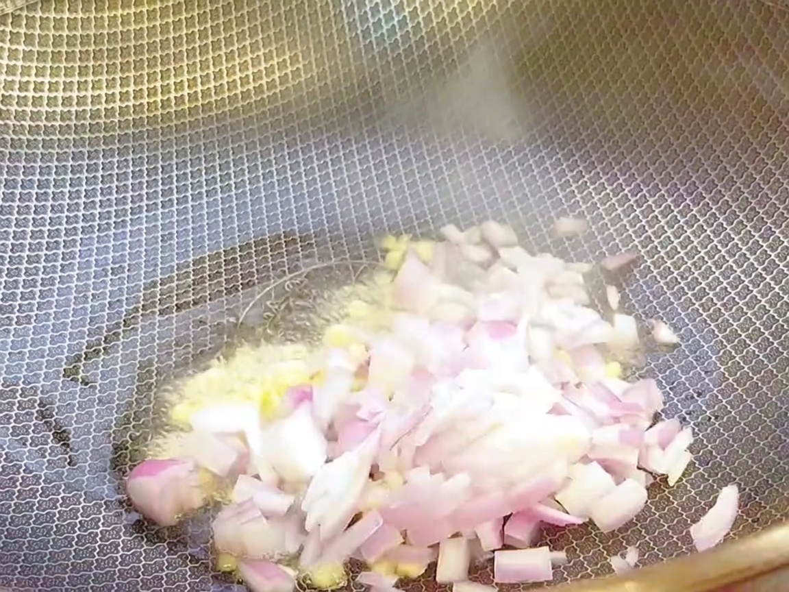 Minced garlic and chopped onions being sautéed in a hot wok with oil.