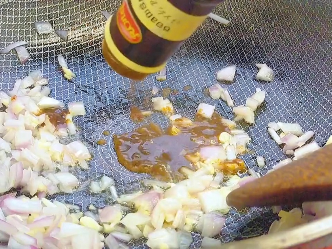 Black pepper sauce being poured from a bottle into a wok over sautéed aromatics.