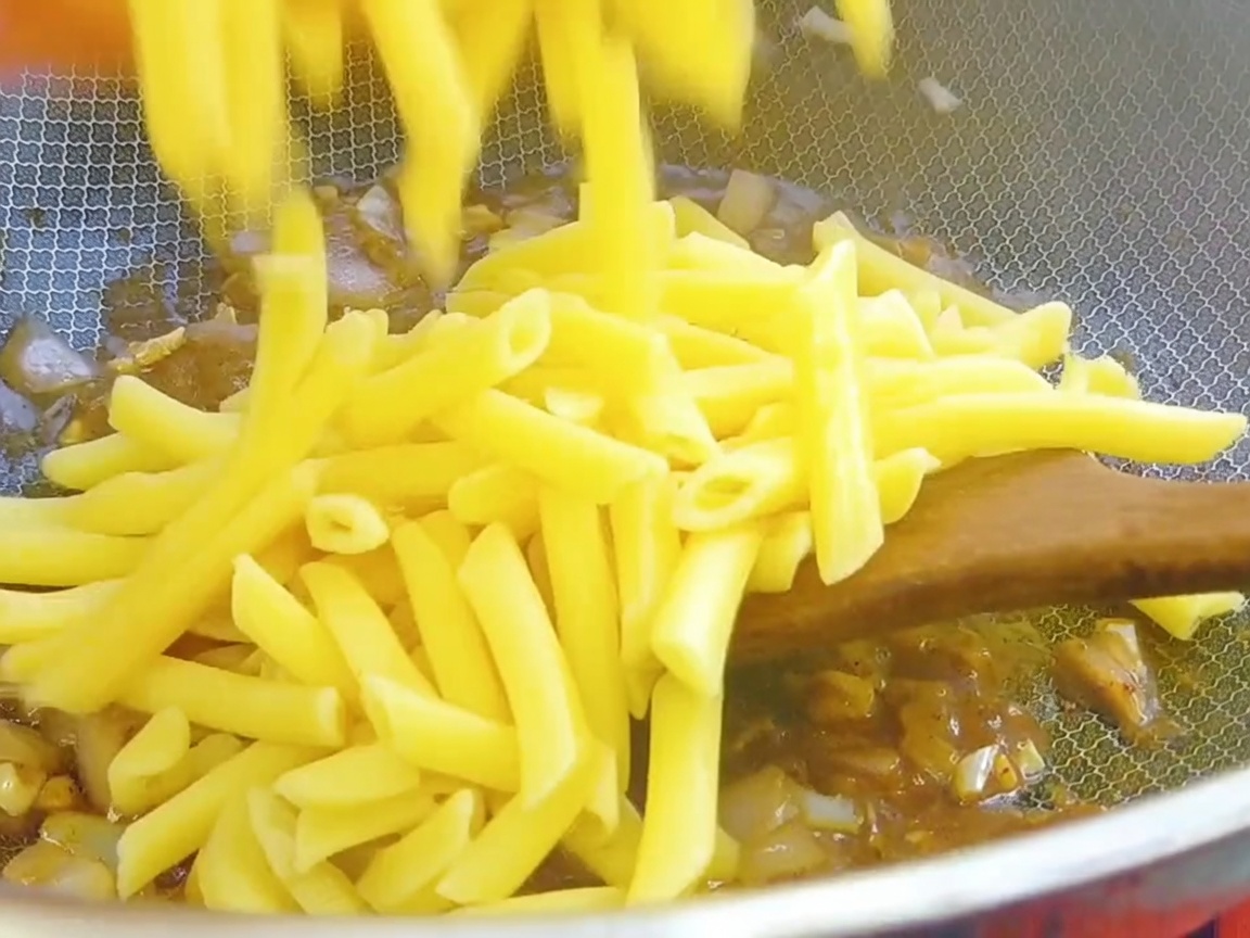 Cooked penne pasta being added to the wok with black pepper sauce base.