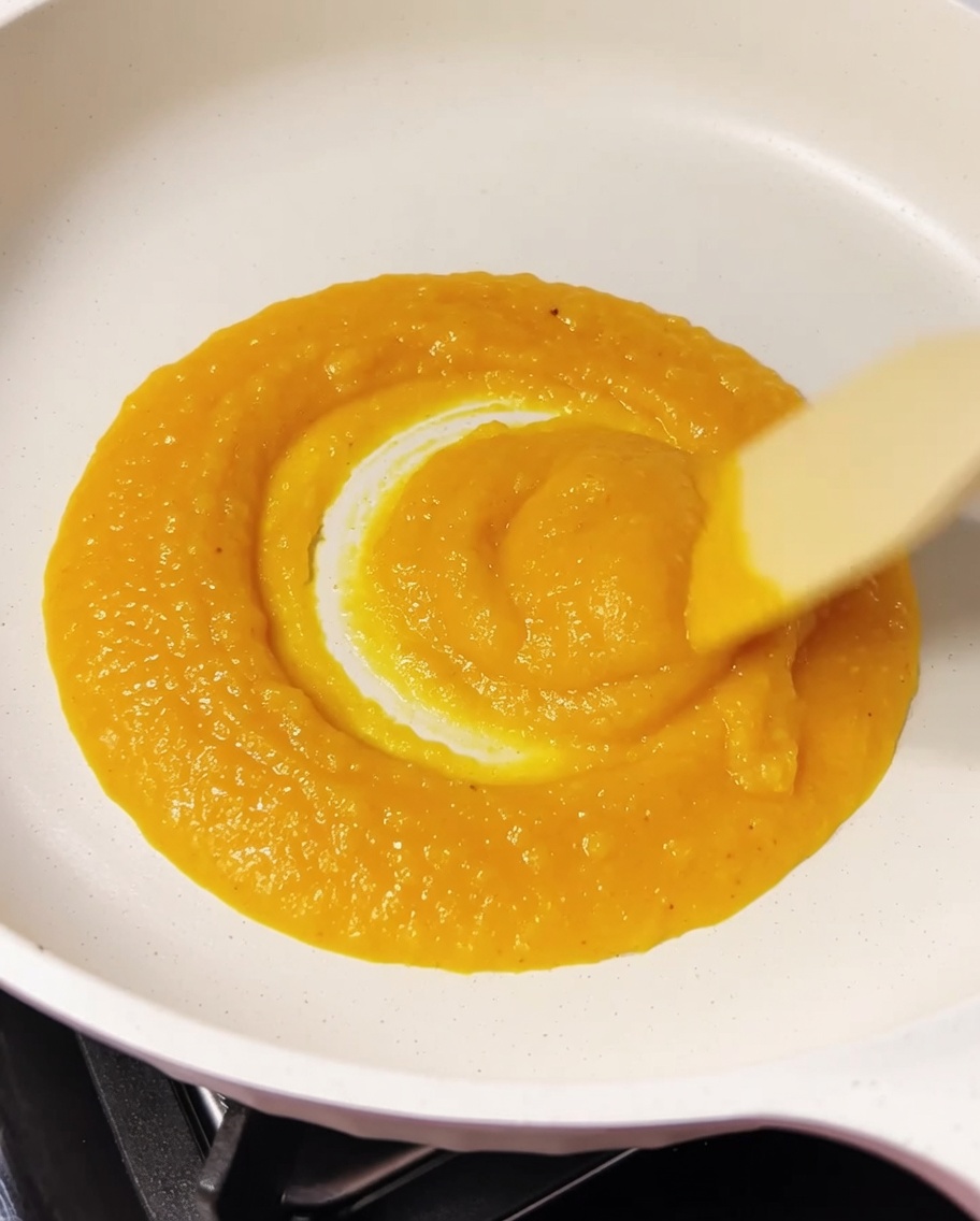 A wooden spatula mixing a golden, creamy mixture of egg yolk and cheese in a white pan.