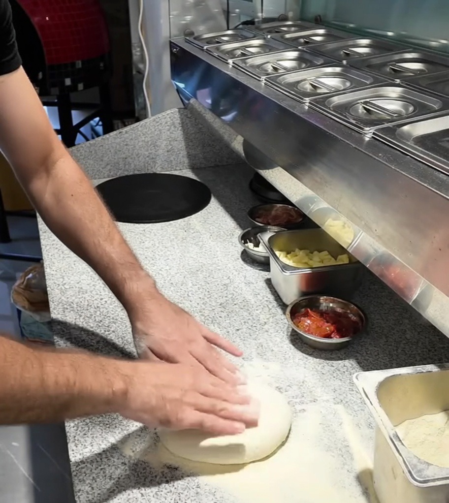 Hands stretching a ball of pizza dough on a floured countertop.