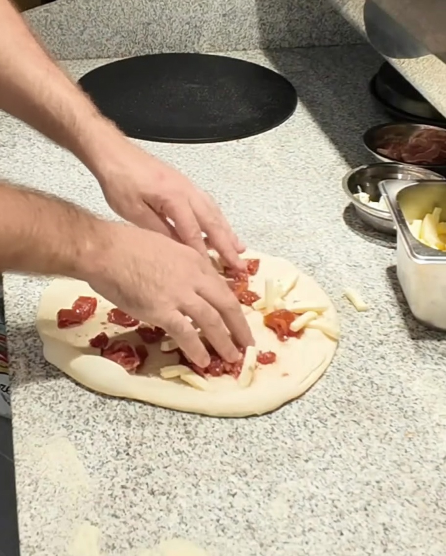 Mozzarella cheese being added to the pizza base.