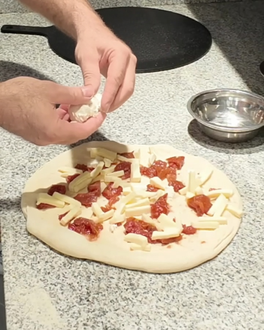 Fresh goat cheese being placed onto the pizza.