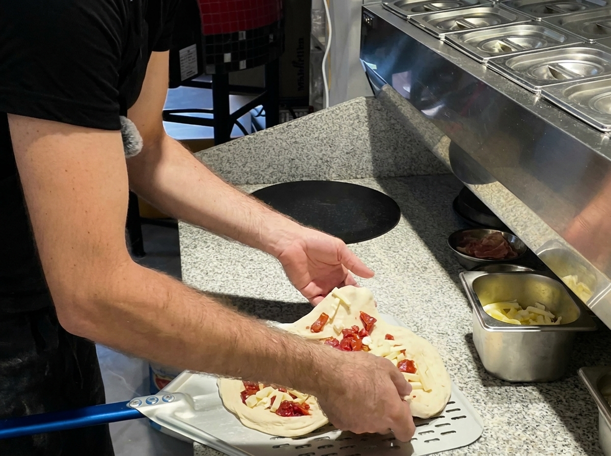 Pizza being slid into an oven on a metal peel.