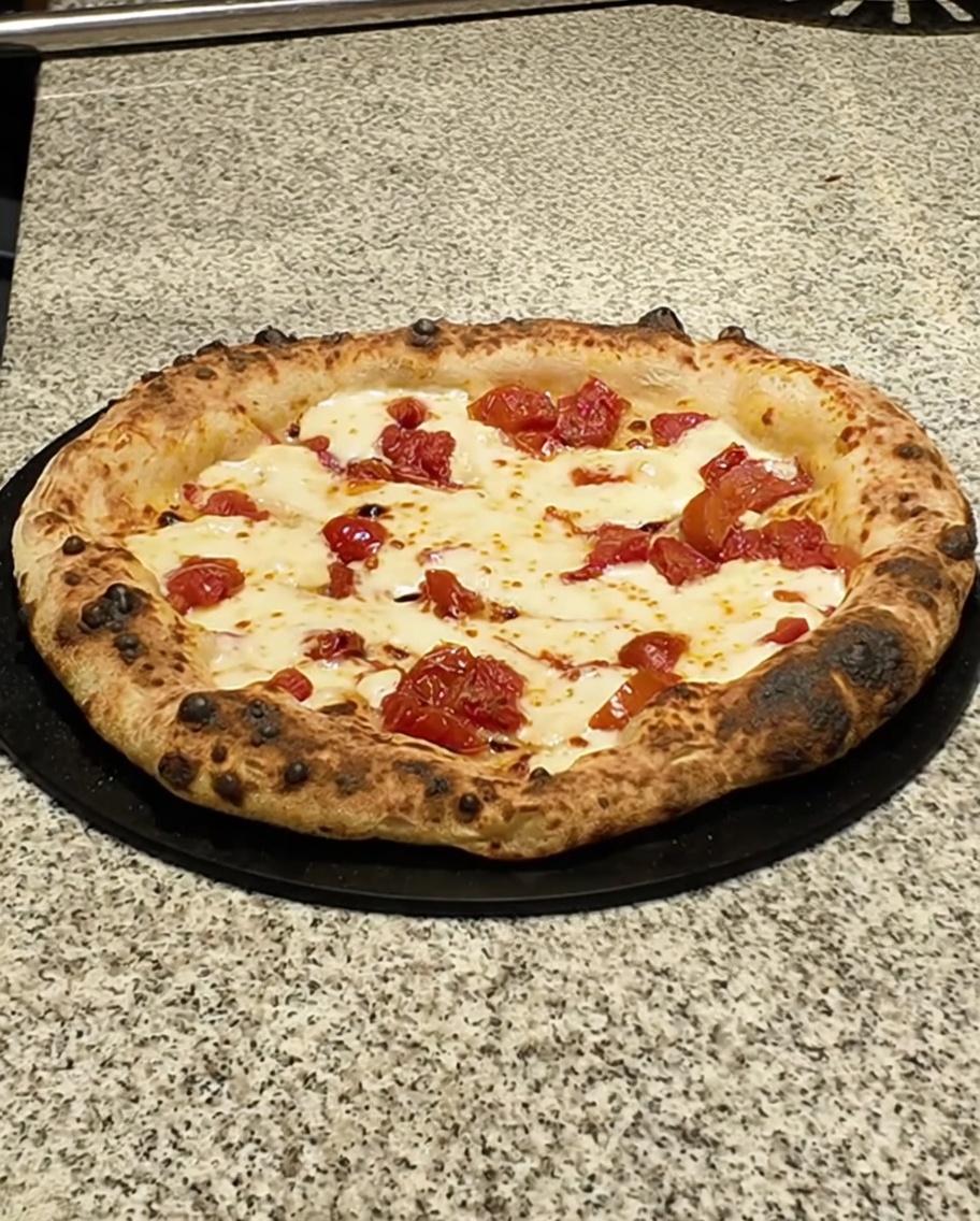 Finished pizza on a dark surface being topped with slices of pancetta.