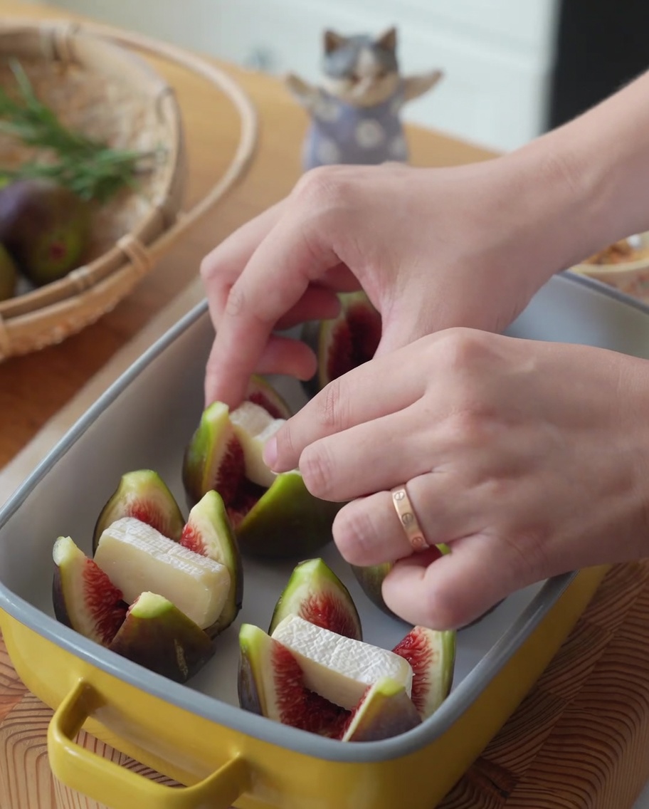 Fig halves in a yellow baking dish being stuffed with pieces of Brie cheese.