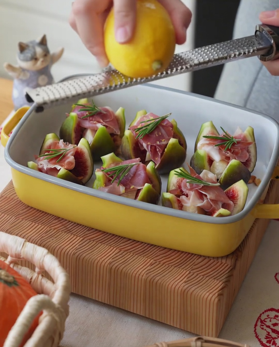 Fresh lemon being zested over a tray of ham-stuffed figs.