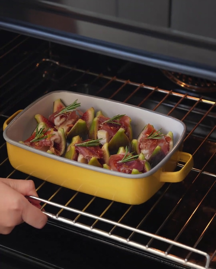 The baking dish containing the figs being slid onto an oven rack.