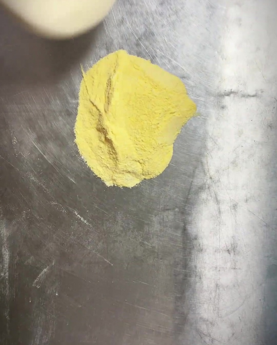 Pizza dough being pressed into a round pan with a visible layer of yellow cornmeal underneath.
