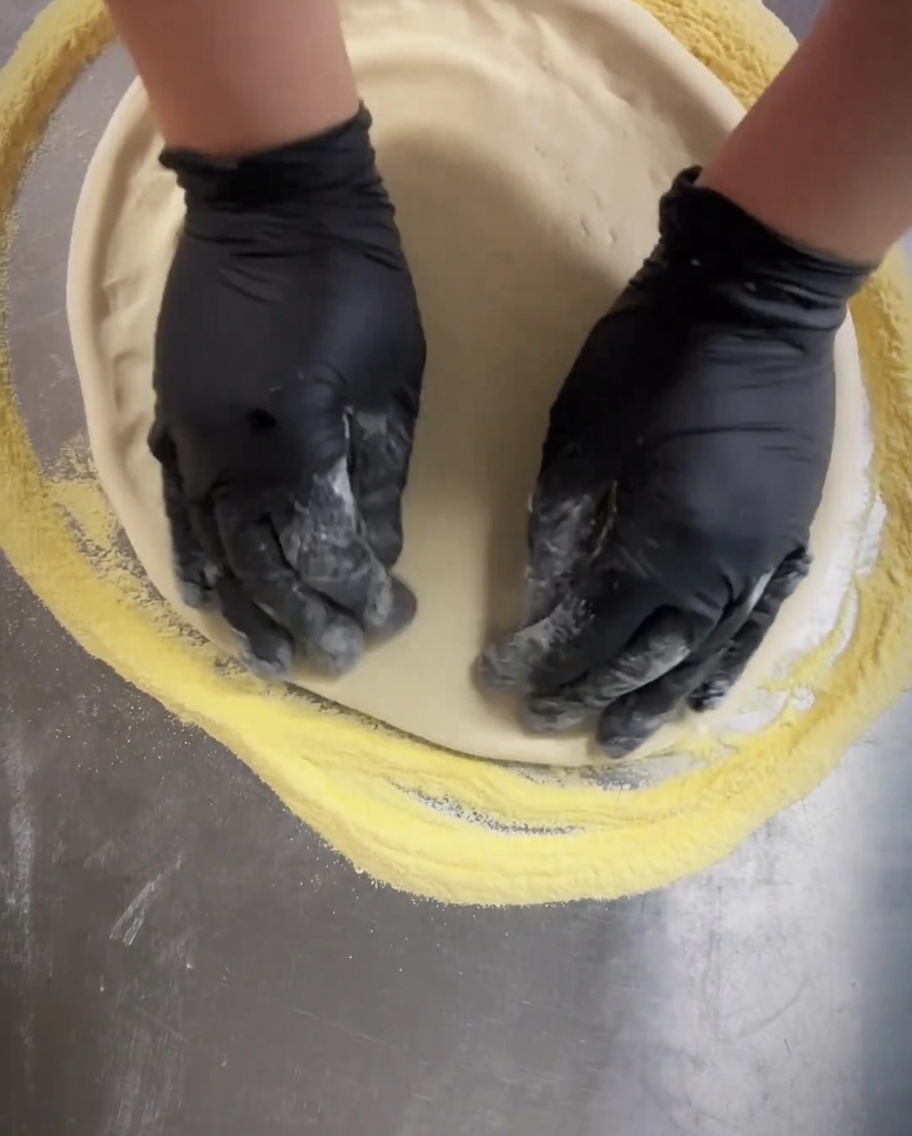 A dough docker tool being rolled across the pizza base to create small, uniform punctures.