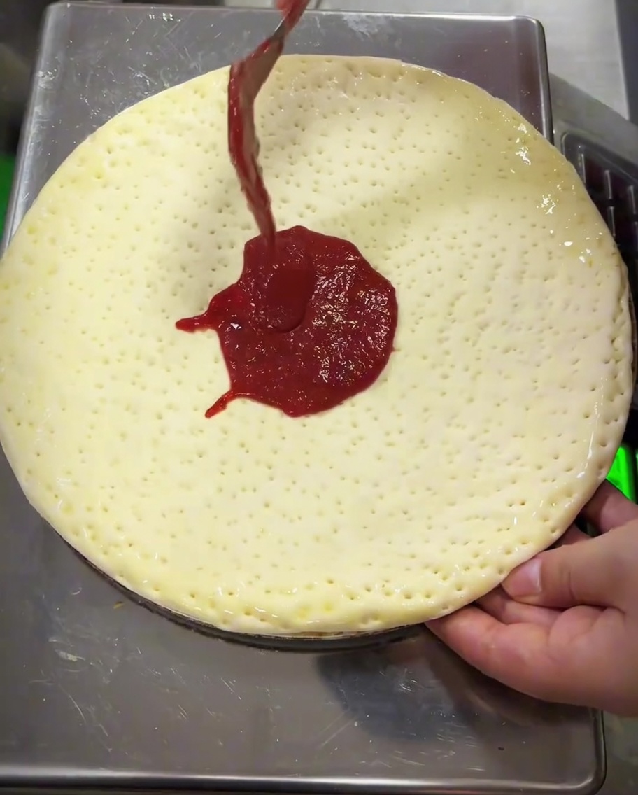 Tomato sauce being spread over the dough using the back of a metal spoon.