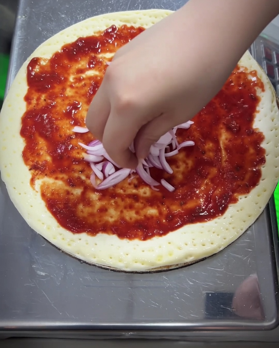 Red onion pieces and a thick layer of shredded mozzarella cheese being added to the pizza.