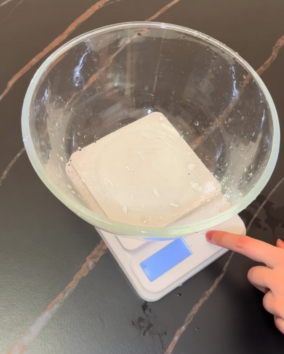 A digital kitchen scale with a glass bowl containing measured flour and dry pizza ingredients.