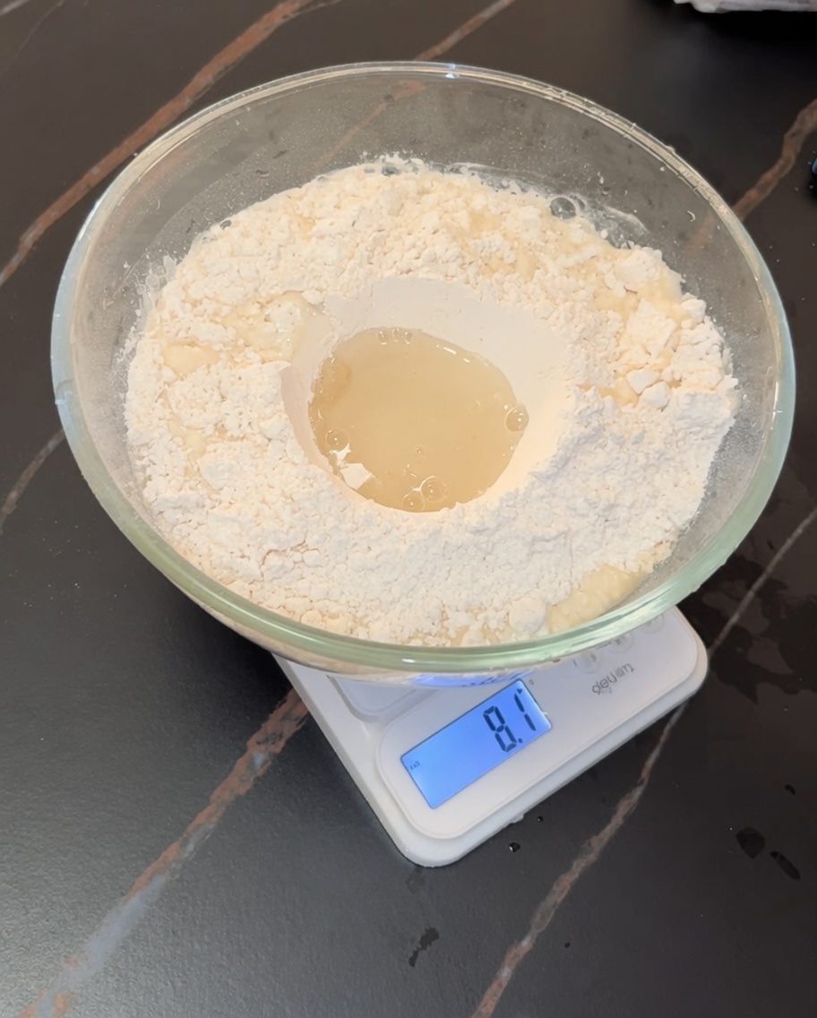 Hands actively kneading a soft pizza dough inside a glass bowl.