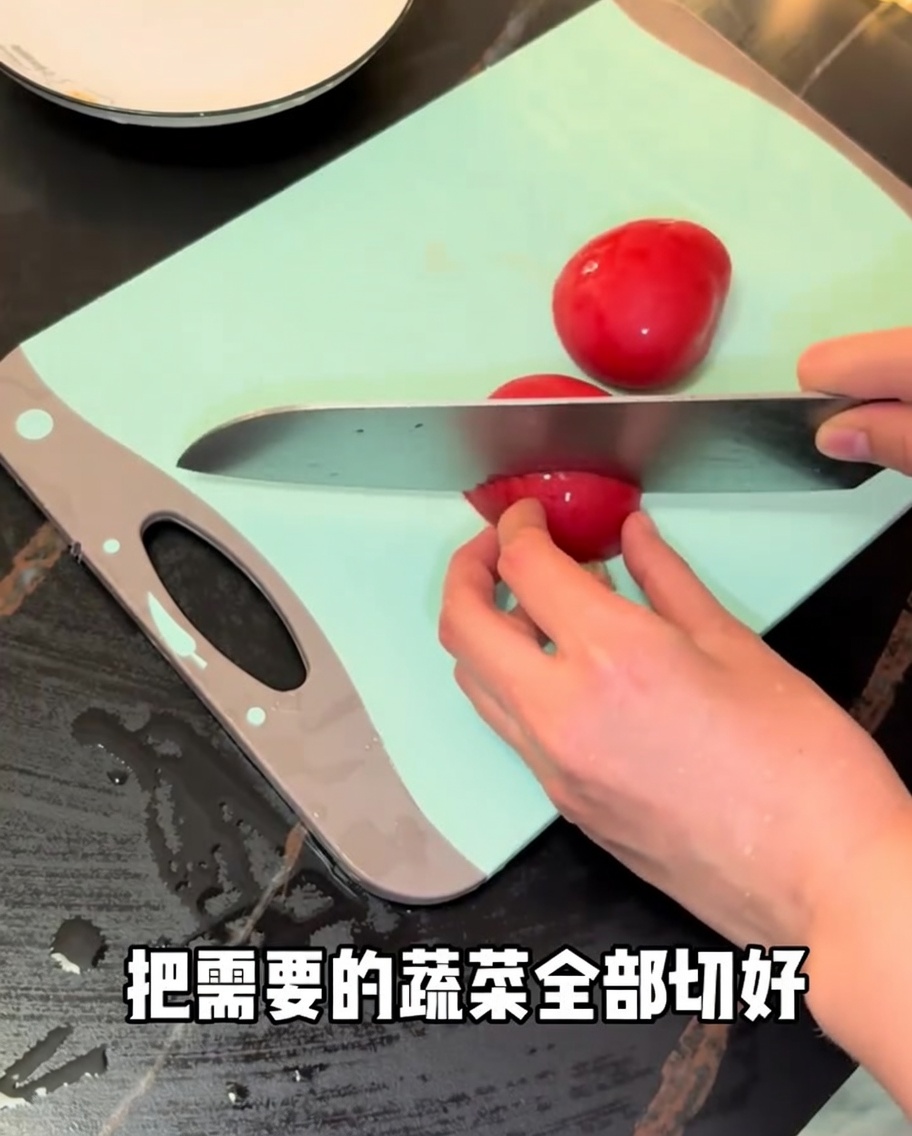 Fresh red tomatoes being sliced with a chefs knife on a green cutting board.