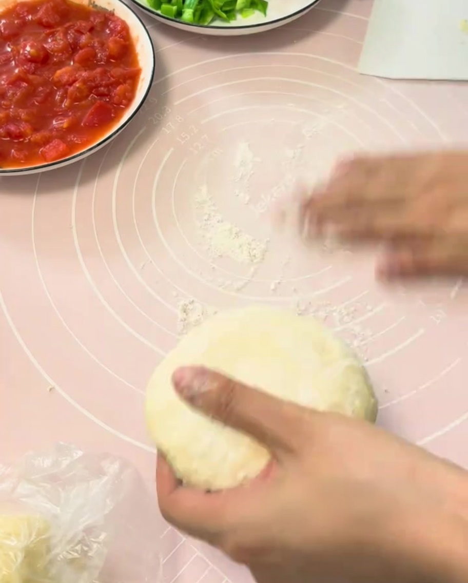 A piece of proofed pizza dough being rolled out flat on a pink silicone pastry mat.
