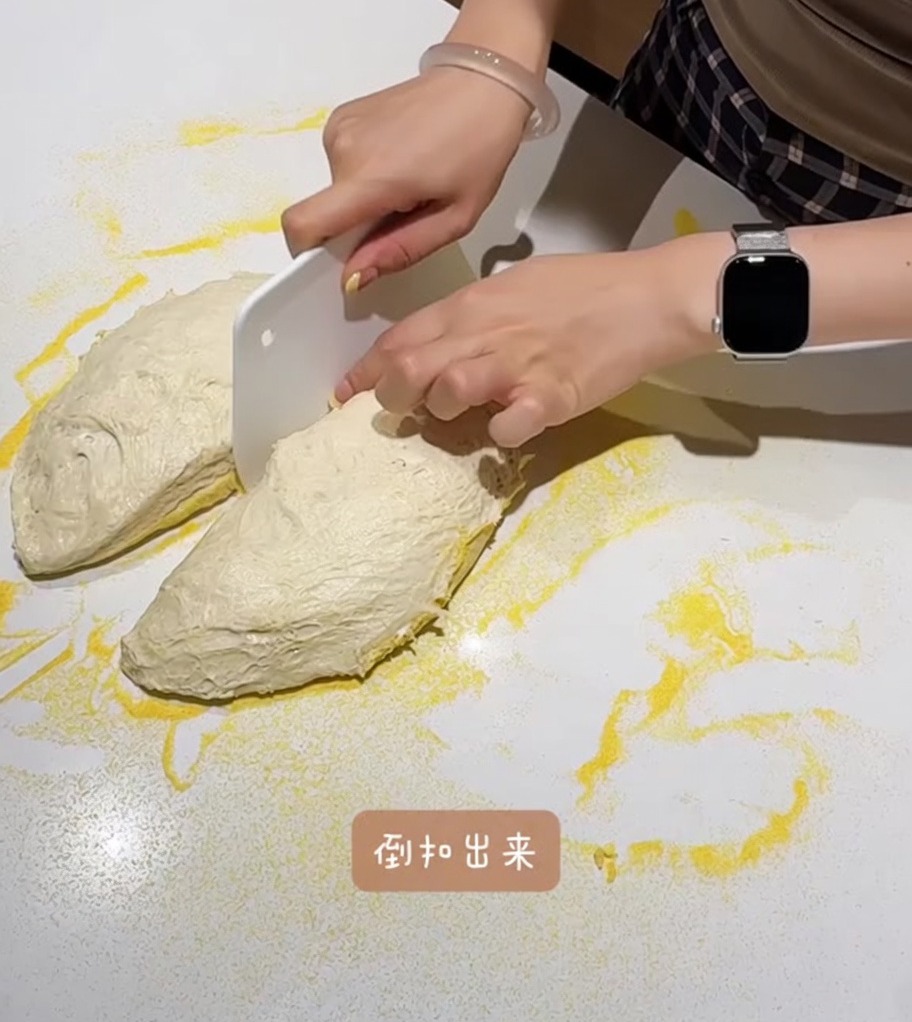 The dough being divided into two equal pieces on a cornmeal-dusted countertop.