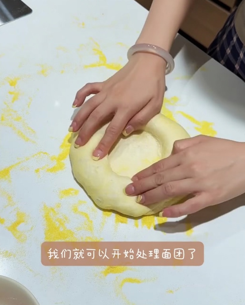 Dough ball being gently pressed and stretched on a work surface, preserving the thick outer rim.
