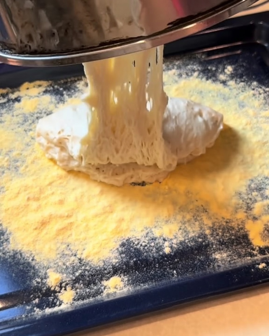 Fermented pizza dough being shaped into a rectangular base on a baking tray.