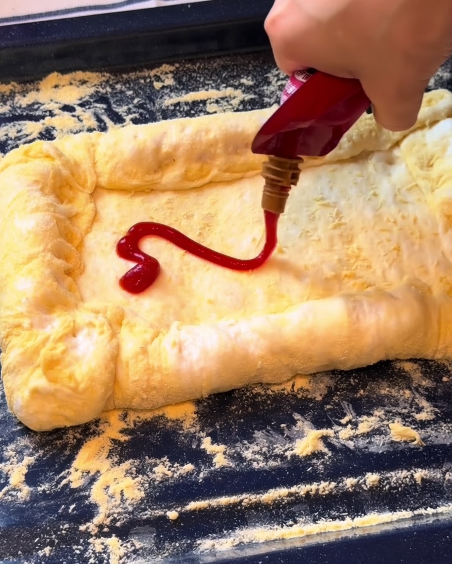 Ketchup being spread on the pizza base followed by a layer of shredded mozzarella cheese.