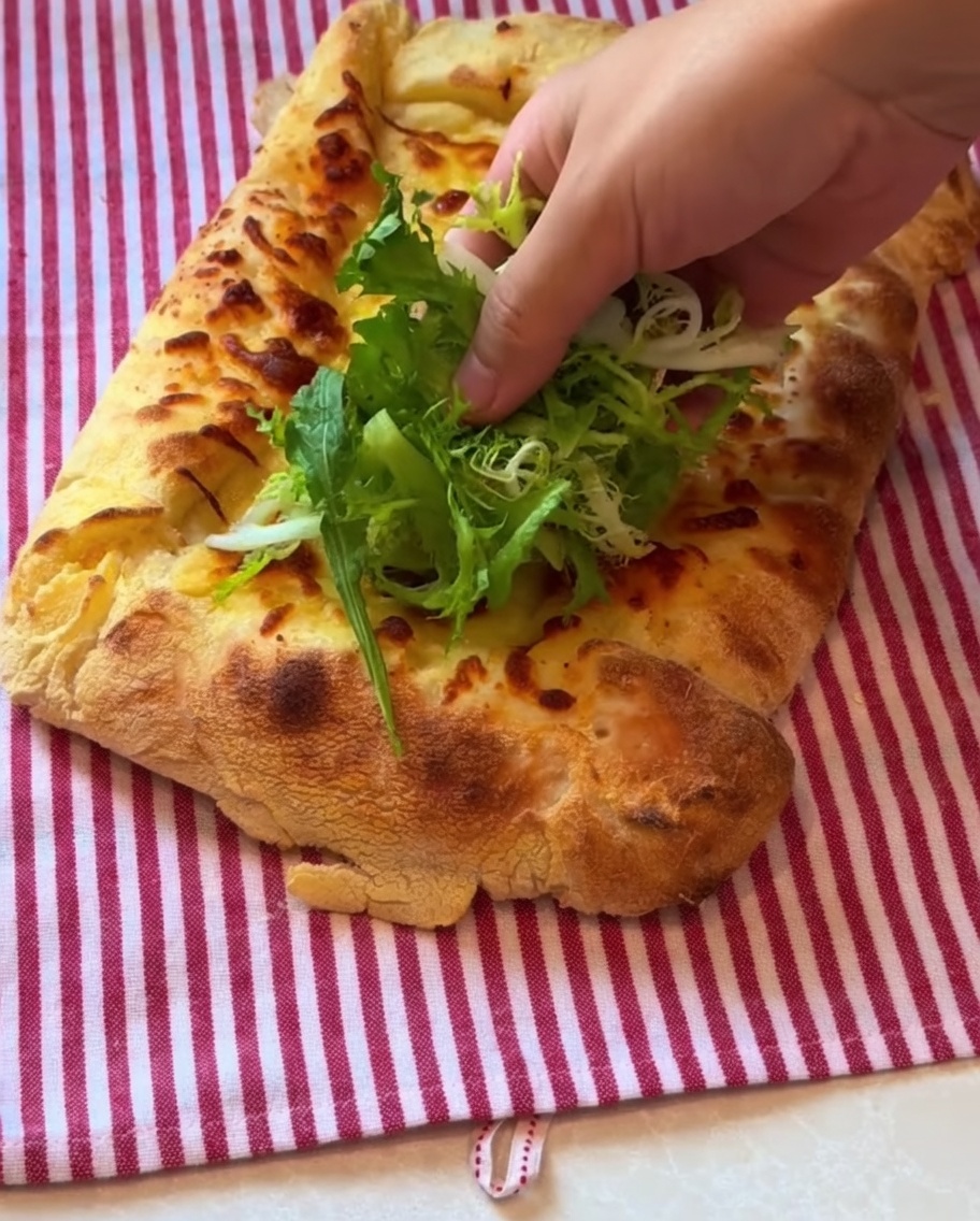 Leafy greens and thinly sliced prosciutto ham being placed on top of the cooked pizza crust.