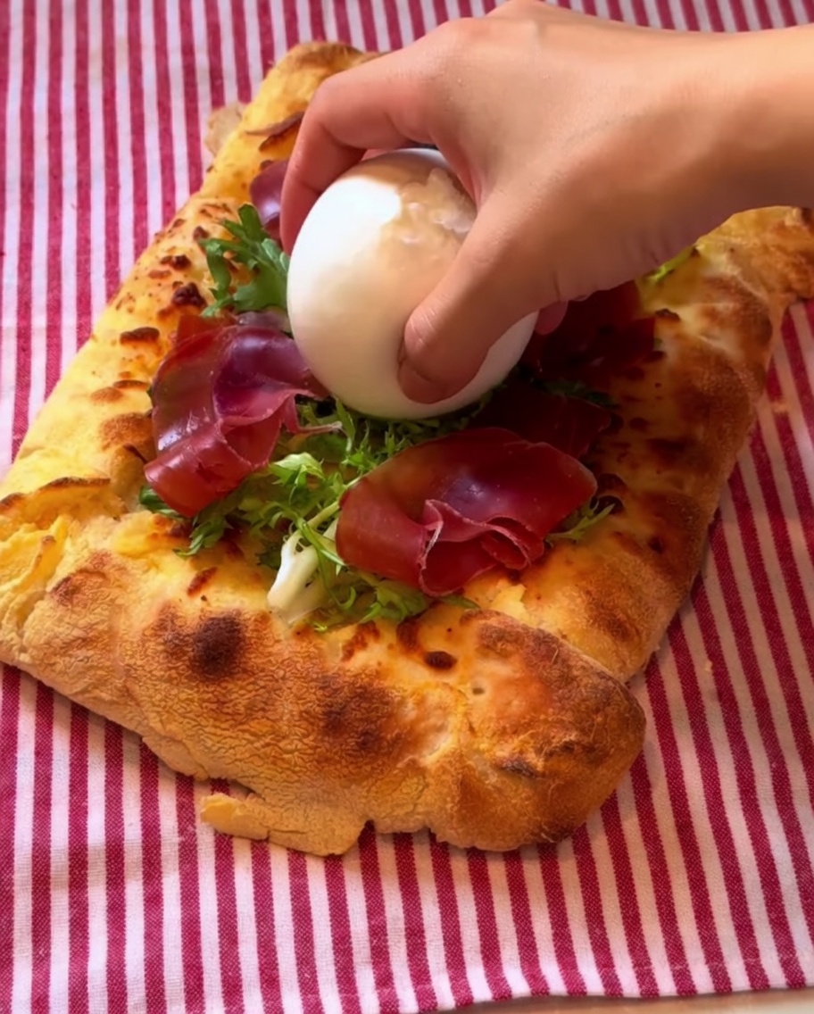 A ball of burrata cheese being placed on the pizza, drizzled with balsamic dressing.