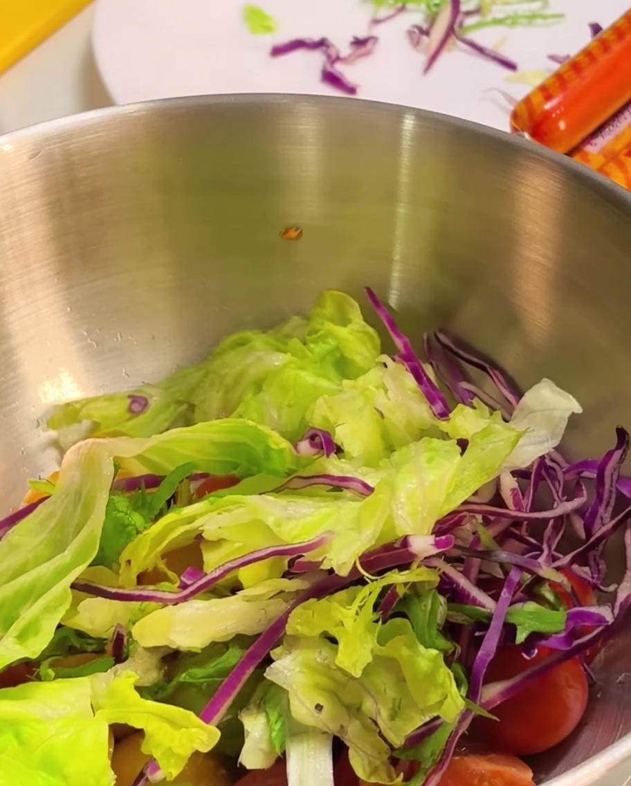 Fresh green lettuce leaves and shredded purple cabbage placed inside a metal mixing bowl over cherry tomatoes.
